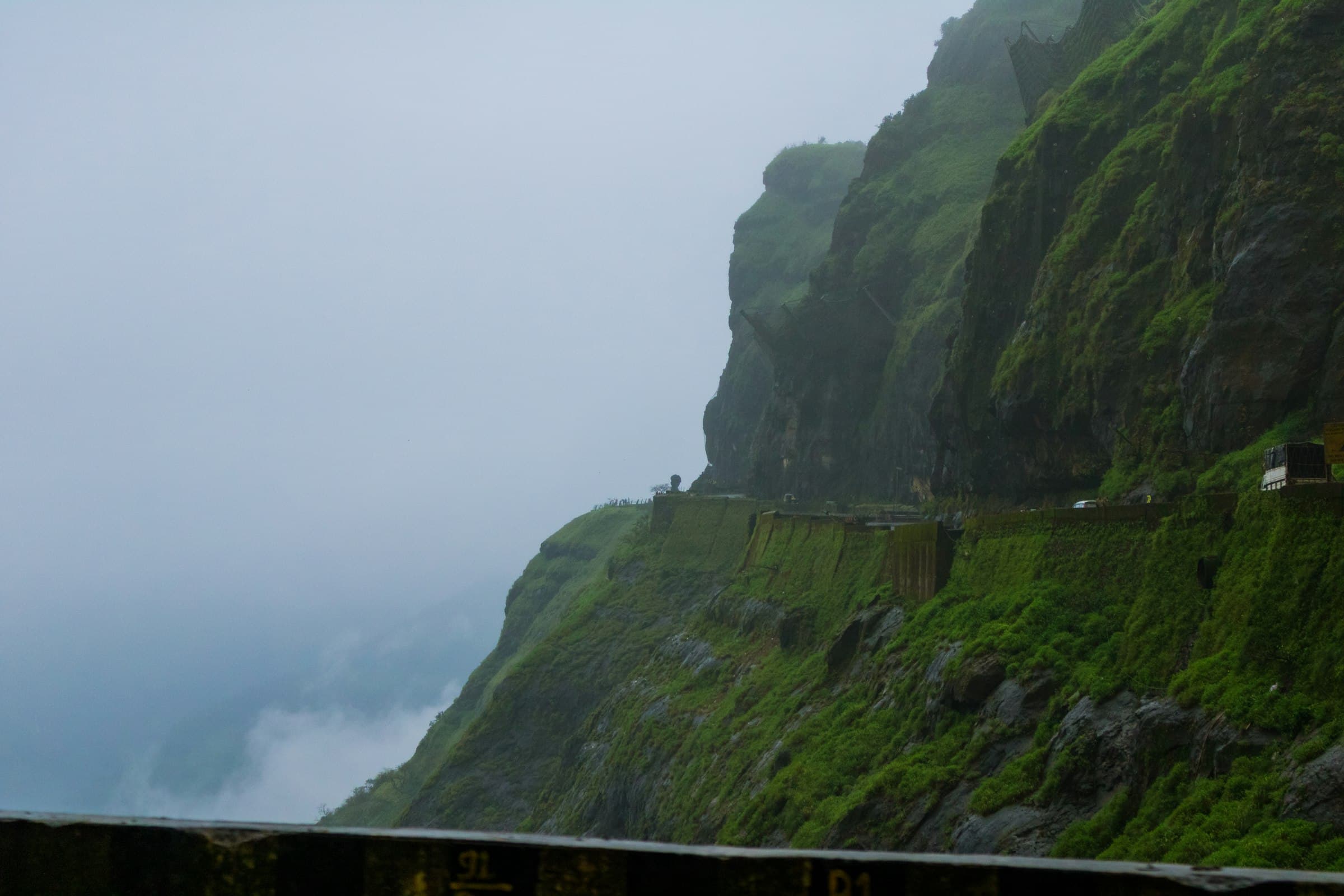 A road winding along green cliffs in monsoon mist